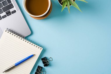 Kahve fincanı, dizüstü bilgisayar klavyesi ve mavi ofis masasında çeşitli kırtasiye malzemeleri. İş ofisi kavramı
