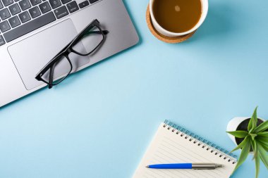 Kahve fincanı, dizüstü bilgisayar klavye ve not defteri mavi ofis masasında. İş ofisi kavramı