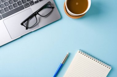 Kahve fincanı, dizüstü bilgisayar klavye ve not defteri mavi ofis masasında. İş ofisi kavramı
