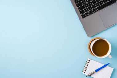 Kahve fincanı, dizüstü bilgisayar klavyesi ve mavi ofis masasında çeşitli kırtasiye malzemeleri. İş ofisi kavramı