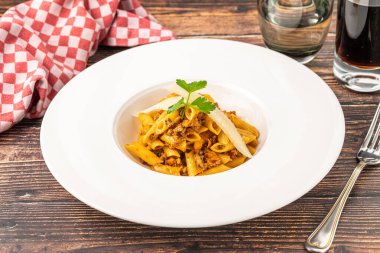 Penne bolonez makarnasının beyaz tabakta, ahşap masada üst görüntüsü.