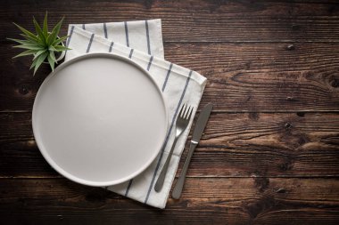 Boş seramik beyaz tabak, çatal ve masa bıçağının ahşap masa üzerindeki üst görüntüsü.