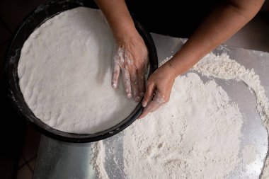 Paslanmaz çelik tezgahta pizza hamuru yapan kadın.