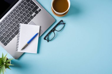 Kahve fincanı, dizüstü bilgisayar klavyesi ve mavi ofis masasında çeşitli kırtasiye malzemeleri. İş ofisi kavramı