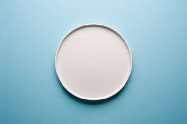 Mavi arkaplanda boş seramik beyaz tabağın üst görünümü