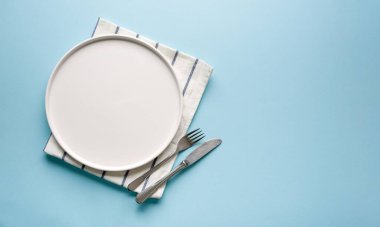 Mavi arkaplanda boş seramik beyaz tabak ve çatal bıçak takımlarının üst görünümü