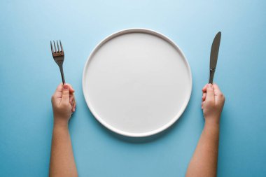 Çatal, bıçak ve mavi arka planda boş tabak tutan kızların üst görüntüsü.