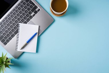 Kahve fincanı, dizüstü bilgisayar klavyesi ve mavi ofis masasında çeşitli kırtasiye malzemeleri. İş ofisi kavramı