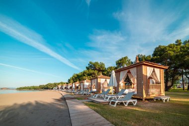 Private beach cabanas on a serene sandy shoreline at sunset clipart