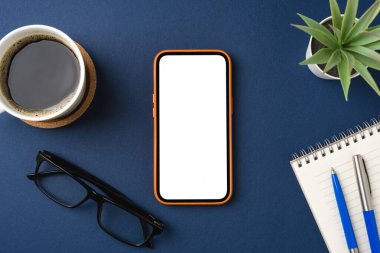 Mavi masadaki boş ekran akıllı telefon. Kahve fincanı, not defteri, kalem ve bardaklar.
