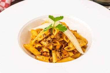 Penne bolonez makarnasının beyaz tabakta, ahşap masada üst görüntüsü.