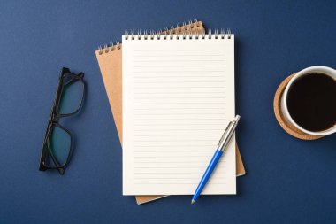 Boş bir defter, kalem, bardak ve kahve ile çalışma alanının üst görüntüsü