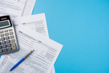 Mavi masadaki vergi formlarının, hesap makinelerinin ve kalemlerin üst görünümü