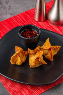 Kırmızı soya soslu siyah bir tabakta kızarmış wonton.