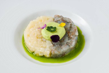Beyaz bir tabakta servis edilen avokado mousse, yenilebilir çiçekler ve yeşil soslu gurme karides ve beyaz balık tartar.