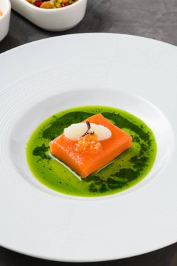 Sous-vide somon fileto ile balık yumurtası, şerbet ve mikro yeşilliklerle süslenmiş, canlı yeşil bitki sosu ile servis edilir.