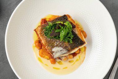 Kızarmış tavada kızartılmış balık fileto, nohut, kremalı sos ve taze yeşillikler.