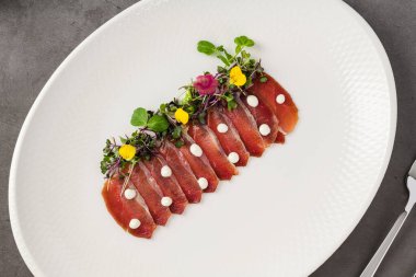 Beyaz porselen tabakta taş masada füme ördek pastırması.