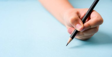 Sol el mavi arkaplanda açık bir defter üzerinde tükenmez kalem tutuyor.