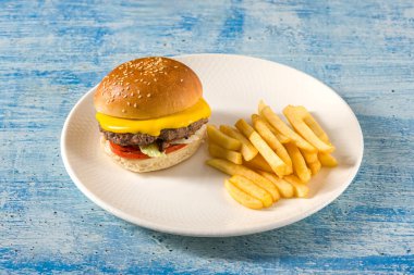 Çedar peynirli ve karamelli soğanlı ezme burger, patates kızartmasıyla servis edilir.