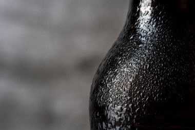 Siyah şişenin üzerindeki su damlalarını gri arka planda yakın plan görüntüsü