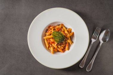 Klasik İtalyan makarna penne alla arrabiata ile fesleğen ve sos koyu gri masada. Baharatlı arrabbiata soslu makarna.