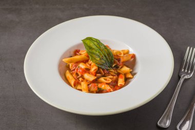 Klasik İtalyan makarna penne alla arrabiata ile fesleğen ve sos koyu gri masada. Baharatlı arrabbiata soslu makarna.