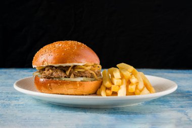 Yavaş Pişmiş Biftek Burger, beyaz bir porselen tabakta patates kızartması.