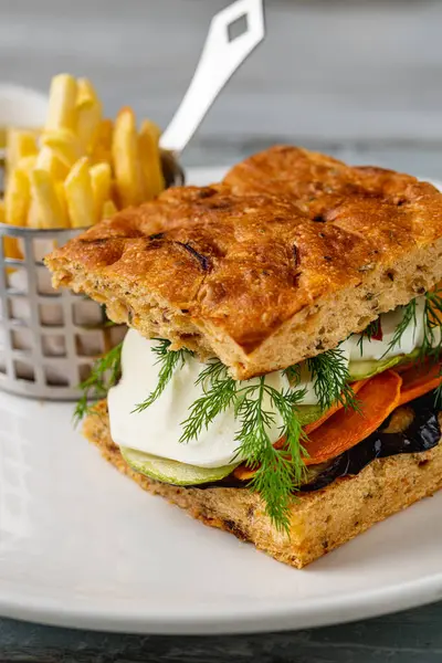 Yanında taze ot ve patates kızartması olan gurme sebzeli sandviç.