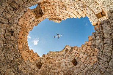 Perge 'nin antik harabeleri berrak mavi gökyüzünde uçan bir uçağı çerçeveliyor.