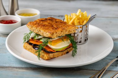 Yanında taze ot ve patates kızartması olan gurme sebzeli sandviç.