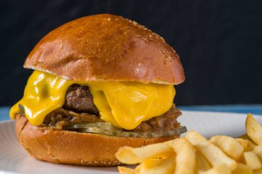 Çedar peynirli ve karamelli soğanlı ezme burger, patates kızartmasıyla servis edilir.