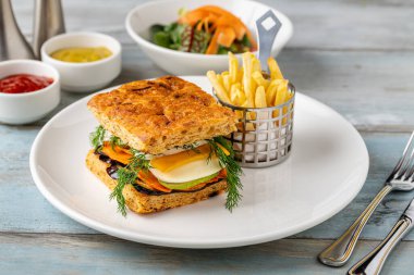 Yanında taze ot ve patates kızartması olan gurme sebzeli sandviç.