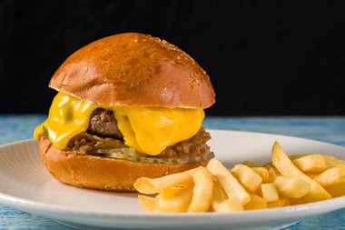 Çedar peynirli ve karamelli soğanlı ezme burger, patates kızartmasıyla servis edilir.