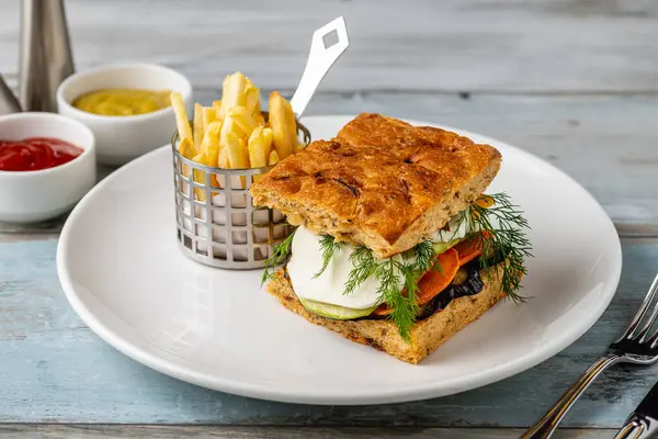 Yanında taze ot ve patates kızartması olan gurme sebzeli sandviç.