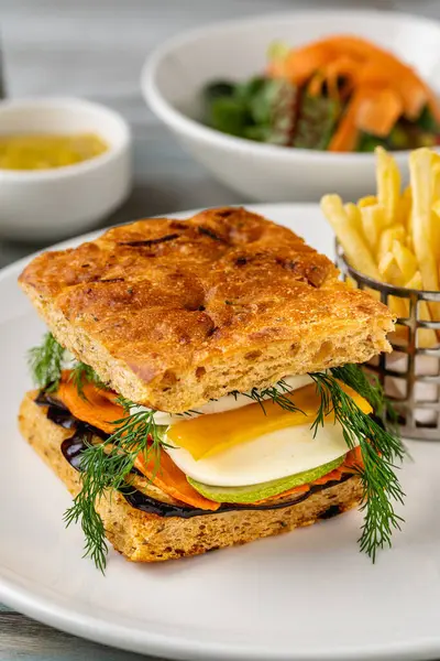 Yanında taze ot ve patates kızartması olan gurme sebzeli sandviç.