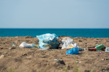 Plastik torbalar ve şişeler deniz kenarındaki kumlu bir plaja atıldı.