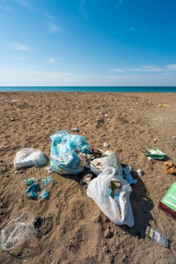 Plastik torbalar ve şişeler deniz kenarındaki kumlu bir plaja atıldı.