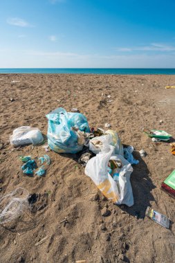 Plastik torbalar ve şişeler deniz kenarındaki kumlu bir plaja atıldı.