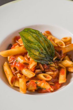 Klasik İtalyan makarna penne alla arrabiata ile fesleğen ve sos koyu gri masada. Baharatlı arrabbiata soslu makarna.