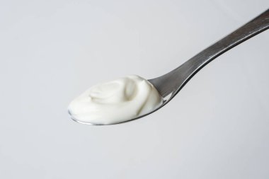 Beyaz arka planda bir kaşık sade kremalı yoğurt.