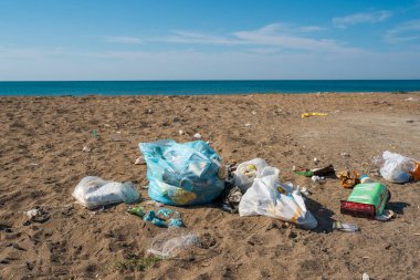 Plastik torbalar ve şişeler deniz kenarındaki kumlu bir plaja atıldı.