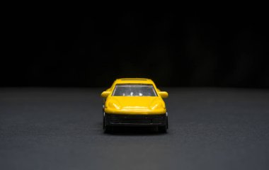 Keskin detayları ve koyu arkaplanı olan sarı oyuncak arabanın ön görüntüsü