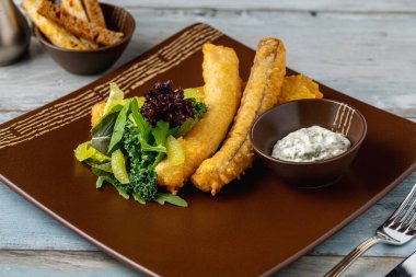 Yeşil salata ve tartar soslu kızarmış balık filetosu.