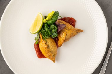 Domates soslu et börekleri, taze yeşillik ve limon dilimi ile servis ediliyor.