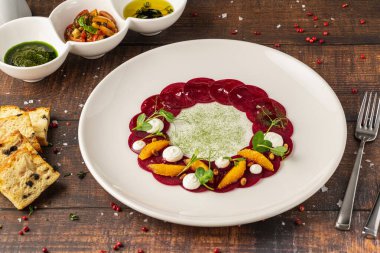 Portakal dilimli pancar carpaccio, taze yeşillikler ve krema noktaları.