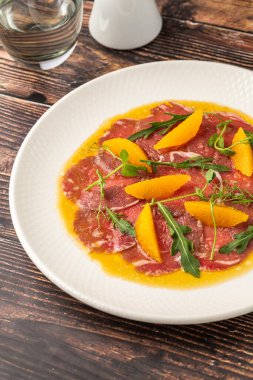 İnce dilimlenmiş et carpaccio portakal dilimleri ve roka yapraklarıyla.