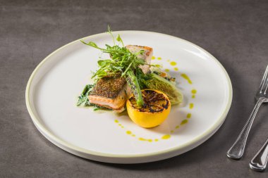 Izgara somon fileto, kömürleşmiş limon ve tabakta yeşillikler.