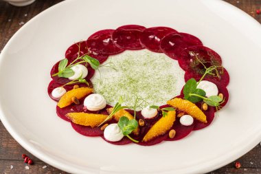 Portakal dilimli pancar carpaccio, taze yeşillikler ve krema noktaları.