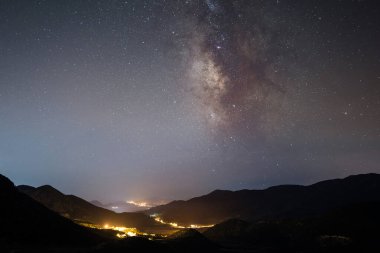 Samanyolu Galaksisi dağların üzerinde ve geceleri parlayan köy ışıkları